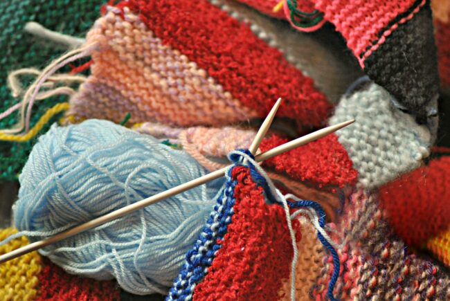 knitting needs surrounded by yarn and partially finished knitting projects